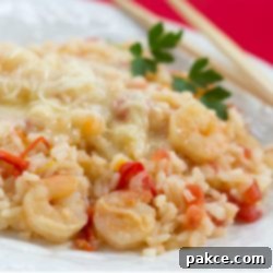 Shrimp and Rice Delight One-Pot Wonder 2 Close-up of a white plate featuring a generous serving of savory one-pot shrimp and rice, garnished with vibrant bell peppers, diced tomatoes, and a generous layer of melted Monterey Jack cheese.