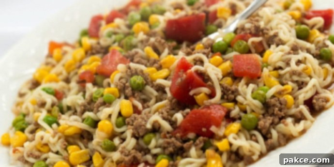 A delicious skillet ramen dish with ground beef, corn, peas, and diced tomatoes, served on a white plate, highlighting a quick and easy one-pan meal.