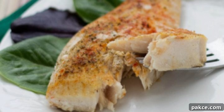 Seasoned fish fillet on a white plate with a fork lifting one bite, showcasing its flaky texture.