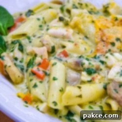 Creamy Florentine Three-Cheese Penne 2 Penne pasta with mushrooms, diced red bell pepper, chopped spinach, and cubed chicken in a cream of chicken sauce, topped with shredded cheddar cheese and garnished with two baby spinach leaves on a white plate.