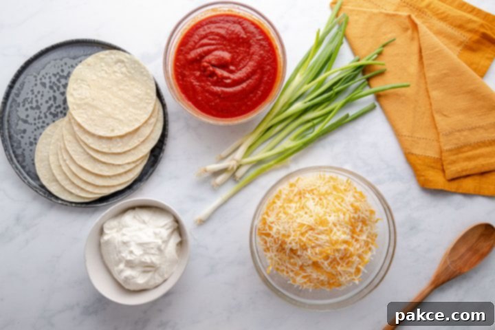Raw ingredients for cheese and onion enchiladas: green onions, sour cream, shredded cheese, and corn tortillas A selection of fresh ingredients laid out: a vibrant bunch of green onions, a tub of creamy sour cream, a bag of shredded Mexican blend cheese, and a stack of corn tortillas, all ready for making delicious enchiladas.