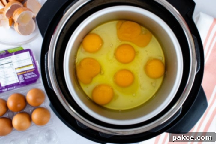 Image showing overhead view of cracked eggs in an inner pot inside Instant Pot with a carton of eggs to the side