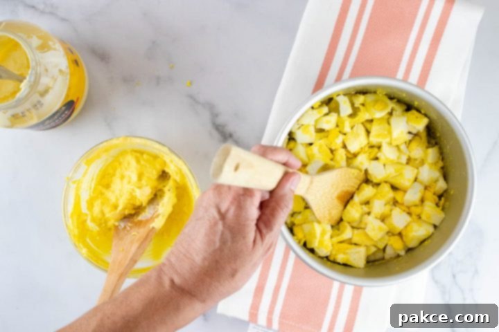 Overhead view of hard boiled eggs being broken up with a wooden spatula with a separate bowl containing a mayonnaise and yolk mixture