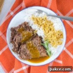 Foolproof Slow Cooker Roast Beef and Gravy 2 a white plate half full of roast beef and half full of rice. Roast beef and rice are both covered with gravy. There is a fork on the plate next to the rice. The plate is on an orange napkin with white stripes.