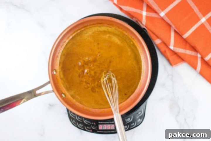 Crockpot Roast Beef & Gravy Overhead shot of a small orange skillet of brown gravy over a warming unit on a white marble counter.There is a whisk in the skillet, and an orange napkin with white stripes on the counter at the top right of the picture.