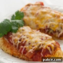 Zesty Santa Fe Chicken 2 Two chicken breasts coated with cracker crumbs, and topped with salsa and melted shredded cheese, on a white plate.