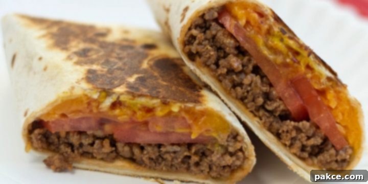 A burrito with ground beef, tomato slices, and melted cheese, cut in half on a white plate, showcasing the delicious filling.