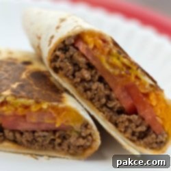 Golden-Crunch Cheeseburger Burritos 2 A beautifully cut Toasted Cheeseburger Burrito on a white plate, revealing its savory ground beef, melted cheese, and fresh tomato filling.
