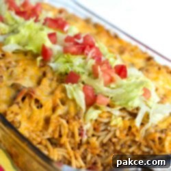 Fiesta Baked Spaghetti 2 Clear casserole dish with spaghetti noodles, ground beef, and melted cheese, topped with shredded lettuce and diced tomatoes.