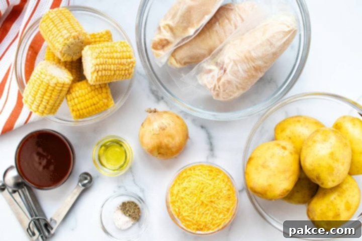 Clear glass bowl with small corn on the cob, clear glass bowl with individually wrapped chicken breasts, clear glass bowl of whole, unpeeled potatoes, bowl of shredded cheddar cheese, bowl with salt and pepper, metal measuring spoons, bowl of barbecue sauce, bowl of oil, and an onion, all on a white marble countertop with an orange and white striped napkin.