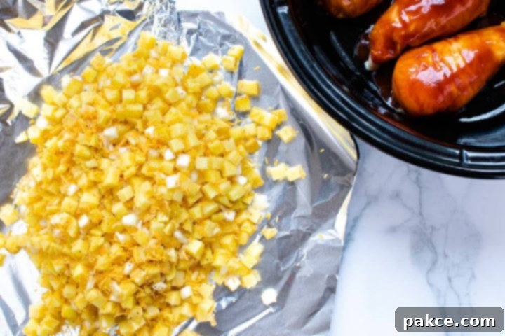 A large piece of foil with diced potatoes, shredded cheddar cheese, and diced onions, beside a slow cooker with chicken breasts in barbecue sauce.