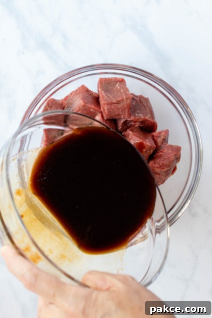 soy-garlic-beef-marinade-ip-2-min Large bowl of homemade soy garlic marinade being poured over another bowl full of cubes of beef, illustrating the marinating process.