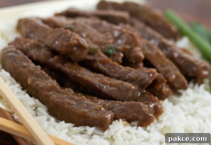 Sliced steak with a sauce on a bed of rice with scallions in the background and chopsticks in the foreground.