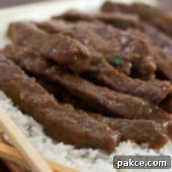Glazed Mongolian Beef Stir-Fry 2 Sliced steak with a sauce on a bed of rice with chopsticks in the foreground.