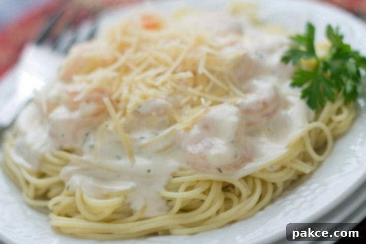 Angel hair pasta with alfredo sauce and shrimp, topped with shredded parmesan cheese, on a white plate.