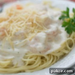 Decadent Garlic Shrimp Angel Hair 2 Angel hair pasta with alfredo sauce and shrimp, topped with shredded parmesan cheese, on a white plate.