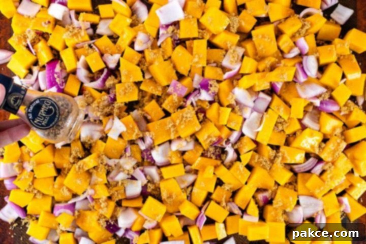 roasted-butternut-squash-candied-pecans-ip-2-min Sheet pan filled with cubed butternut squash and diced red onion, evenly spread and sprinkled with brown sugar and nutmeg, ready for roasting.