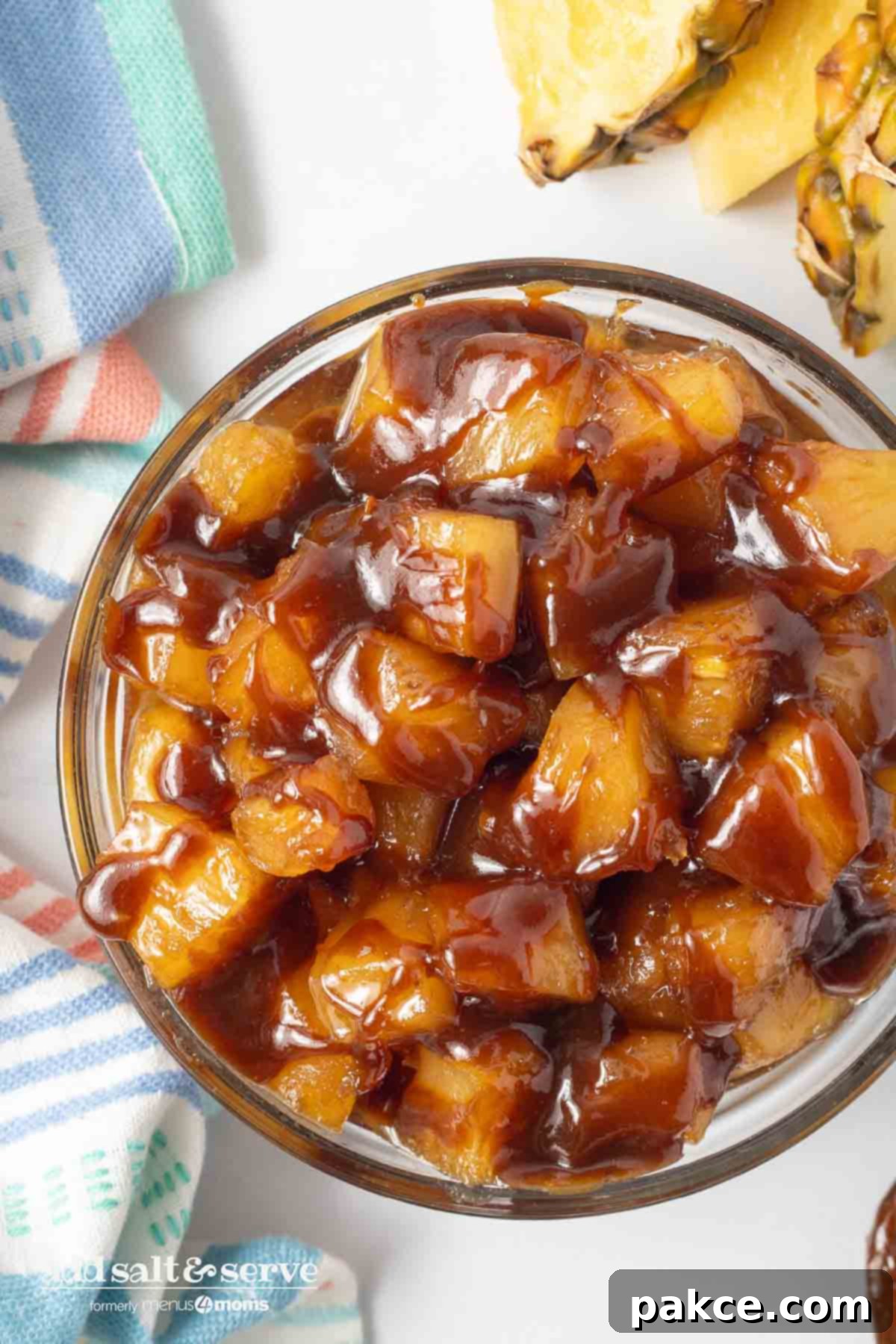 Effortless 3-Ingredient Caramelized Pineapple 7 Bowl of caramelized pineapple chunks beside a tea towel and sliced pineapple on a counter.