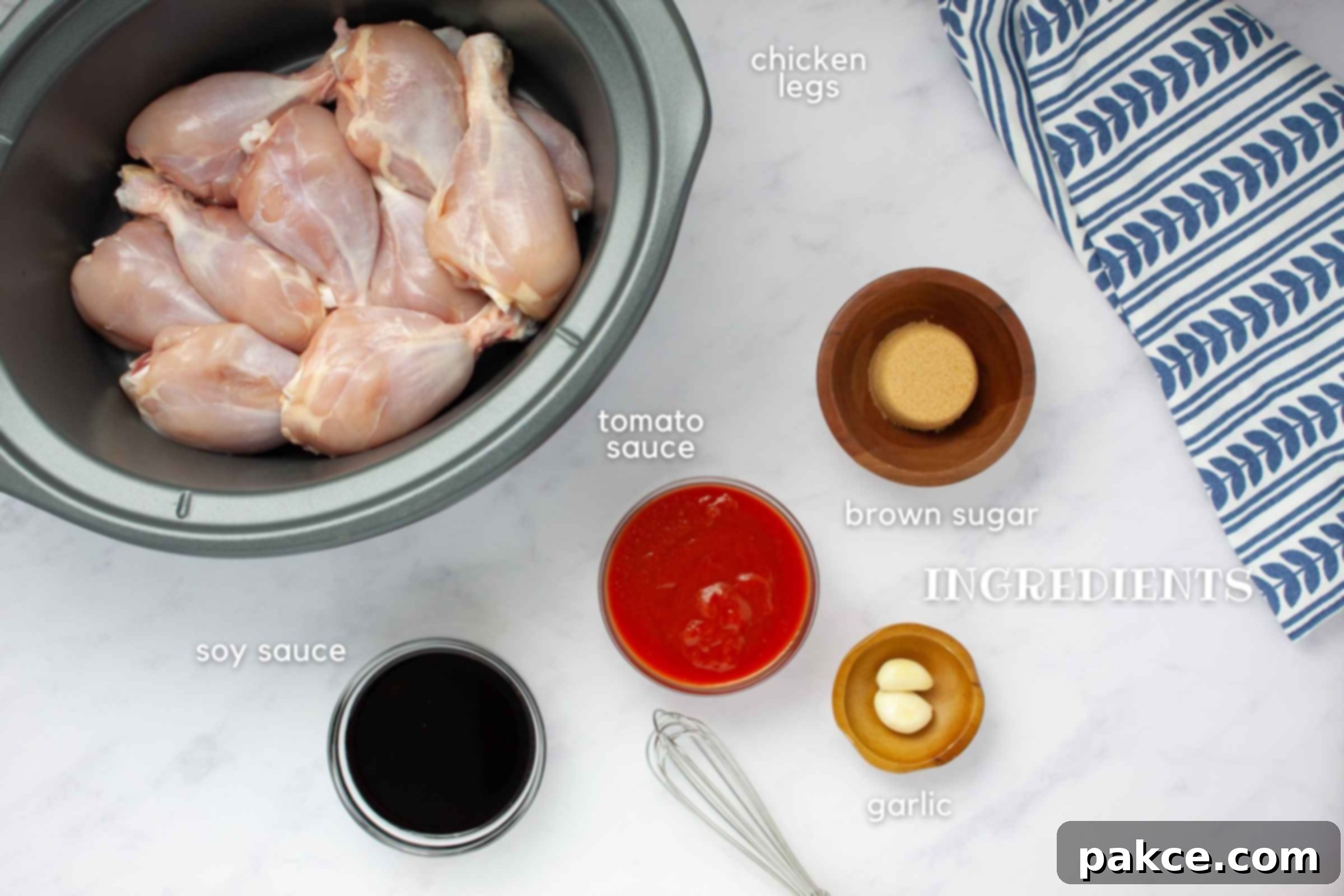 Effortlessly Tender Slow Cooker Chicken Legs 3 Ingredients for slow cooker chicken legs: a pile of skinless chicken drumsticks, a bowl of brown sugar, a can of tomato sauce, a bottle of soy sauce, and fresh garlic cloves arranged on a rustic wooden cutting board.