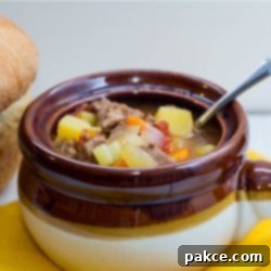 Hearty Slow-Cooked Beef and Vegetable Soup 2 Brown and white soup bowl with vegetable beef soup and a spoon, next to a loaf of bread.