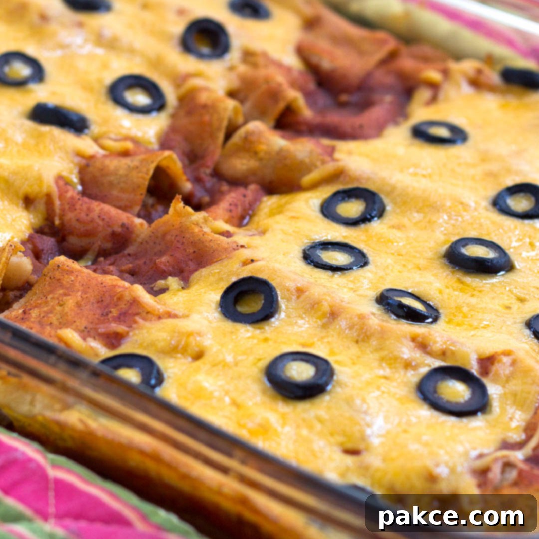 Glass casserole dish with enchiladas topped with melted cheese and sliced black olives.