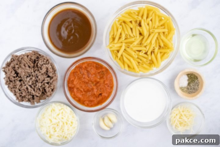freezer-friendly-penne-pasta-bake-ip-1-min Overhead view of ingredients for Penne Pasta Bake: penne pasta, cooked ground beef, spaghetti sauce, brown gravy, garlic, half and half, mozzarella cheese, parmesan cheese, herbs, salt & pepper