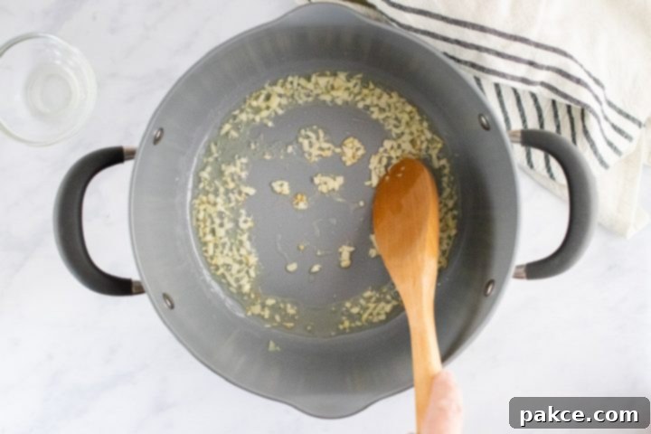 freezer-friendly-penne-pasta-bake-ip-2-min A wooden spoon stirring minced garlic in a pan