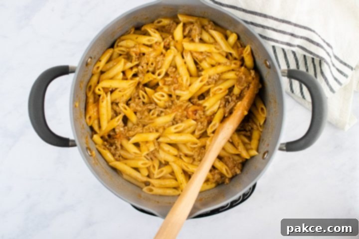 freezer-friendly-penne-pasta-bake-ip-5-min overhead view of cooked penne pasta and cooked ground beef in a creamy sauce in a large pot