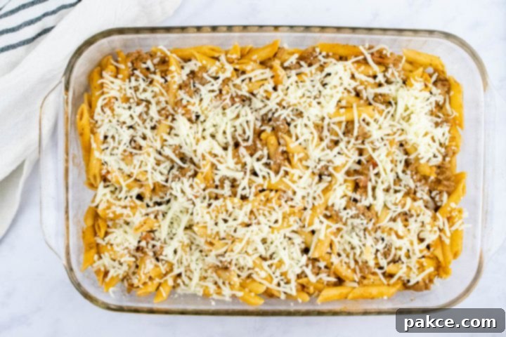 freezer-friendly-penne-pasta-bake-ip-6-min Overhead view of unbaked penne pasta bake topped with shredded cheese in a glass pan
