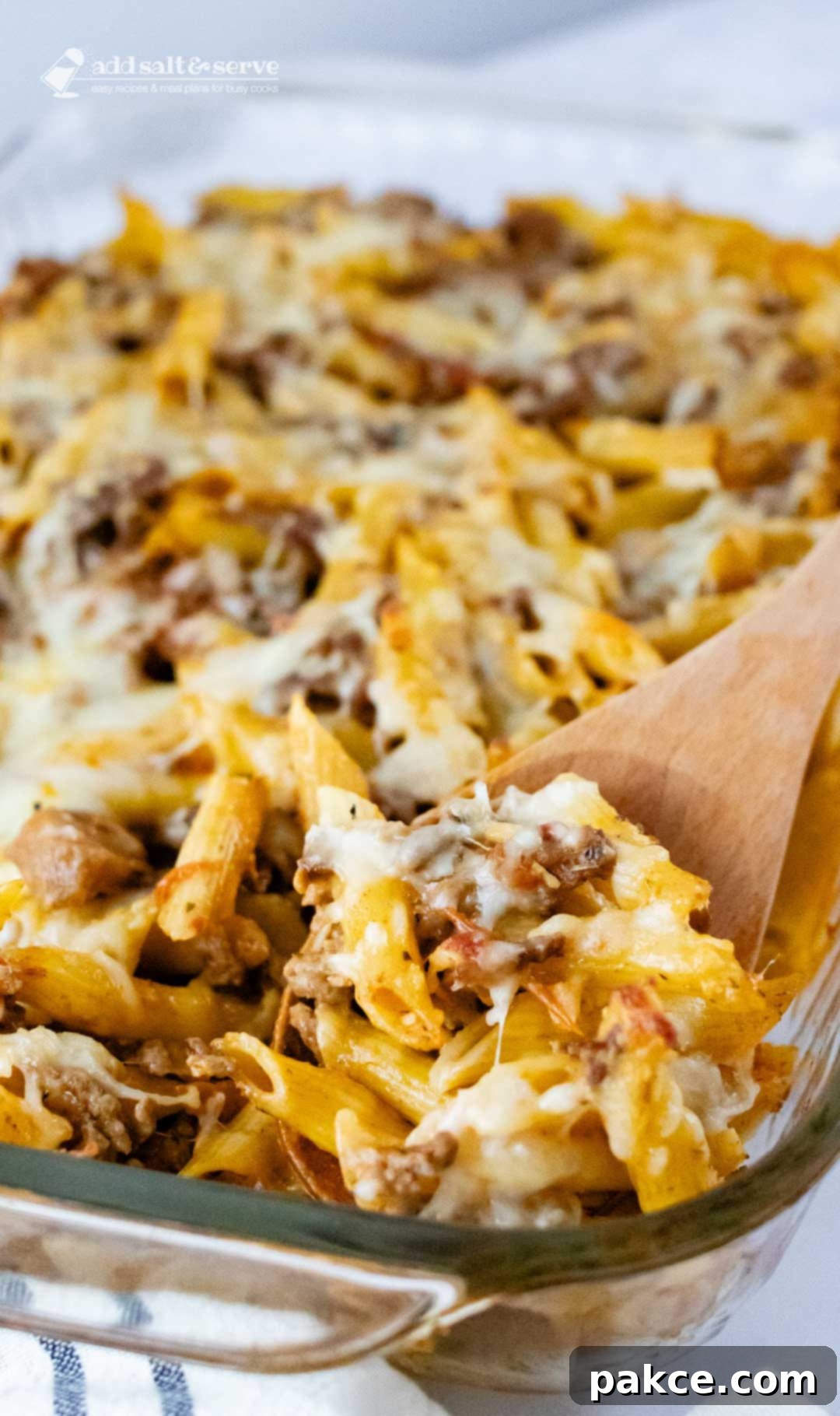 Make Ahead Penne Pasta Bake 3 Overhead view of penne pasta bake topped with melted cheese in a glass pan with a spoonful scooped out and held toward the camera.