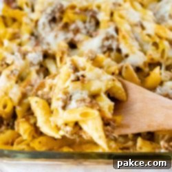 Make Ahead Penne Pasta Bake 4 Side view of penne pasta bake topped with melted cheese in a glass pan with a spoonful scooped out and held toward the camera