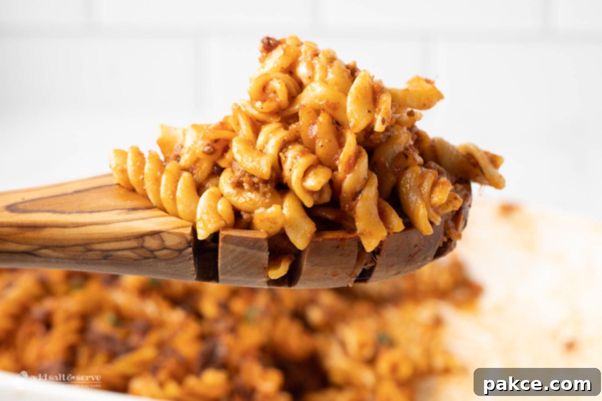 A serving of Cheesy Spiral Pasta Bake on a wooden spoon, fresh from the dish.