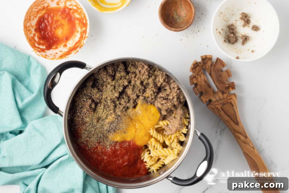 Gooey Golden Spirals 4 Large pot with cooked spiral pasta, cooked ground beef, marinara sauce, condensed cheddar cheese soup, Italian seasoning, and black pepper not yet mixed together.