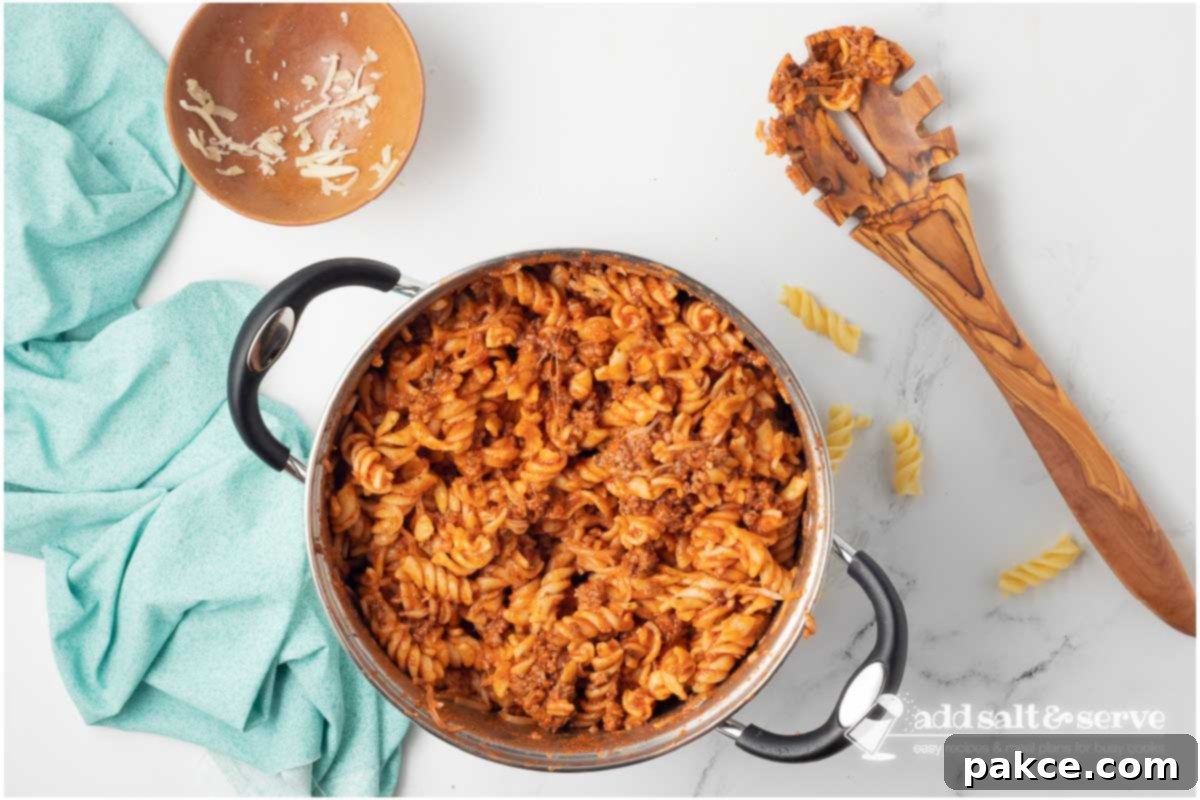 Gooey Golden Spirals 6 Large pot with spiral pasta with cheese and ground beef served in white bowls.