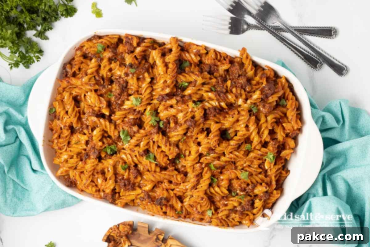 Gooey Golden Spirals 8 Spiral pasta bake in a white casserole dish garnished with fresh parsley.