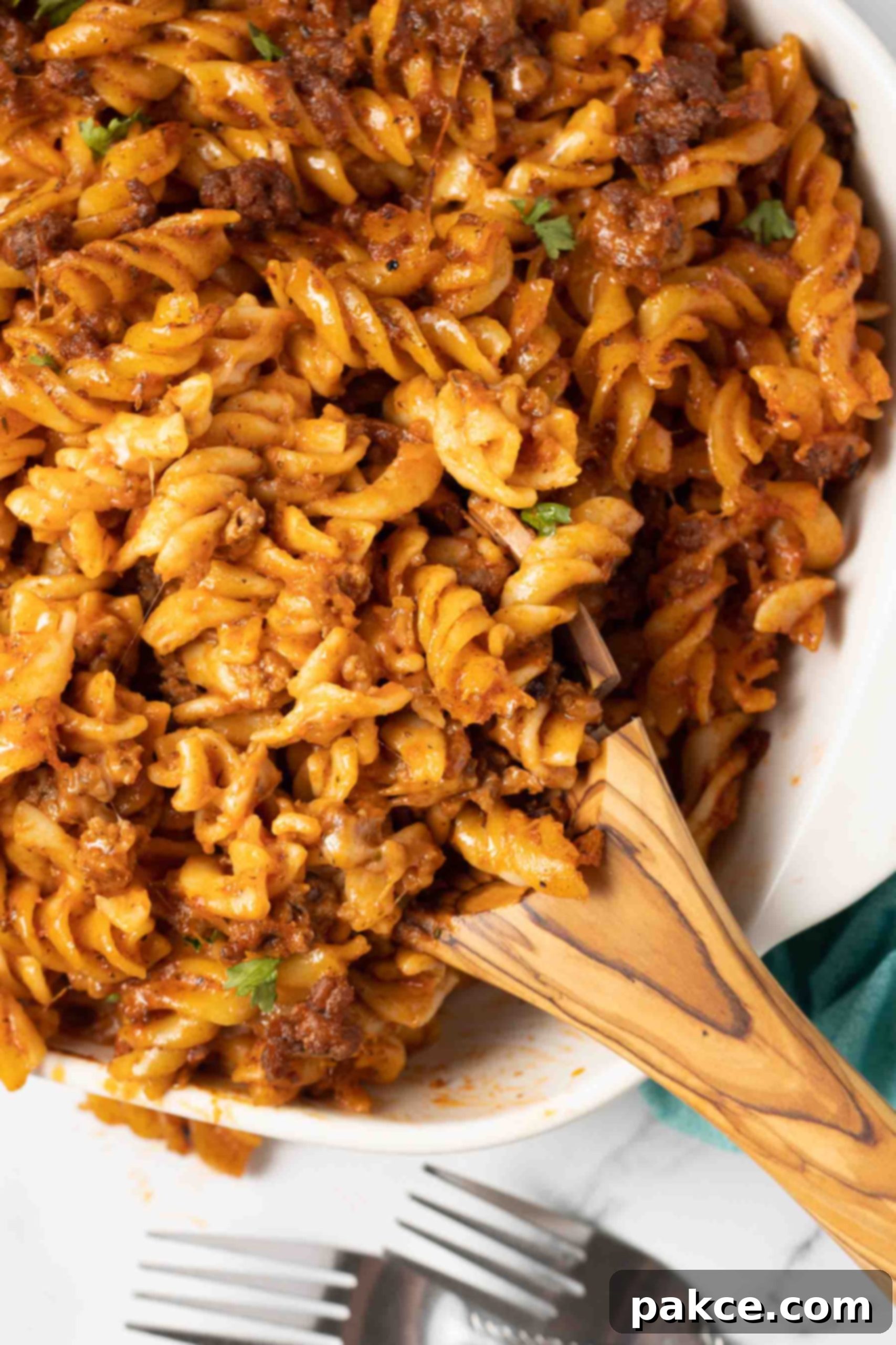 Gooey Golden Spirals 9 Spiral pasta bake in a white casserole dish with a serving on a wooden spoon in the dish.