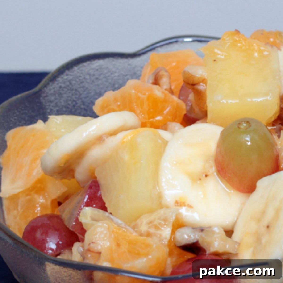 Grapes, chopped oranges, pineapples, and walnuts, and sliced bananas in a bowl.