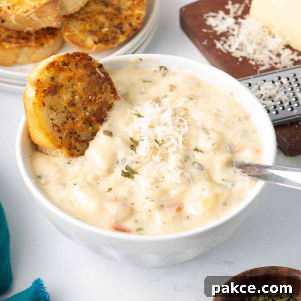 A bowl of Copycat Olive Garden Chicken Gnocchi Soup served with a piece of toasted garlic bread and a wedge of Parmesan cheese with a grater to the side.