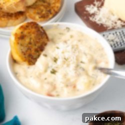 Recreate Olive Garden's Chicken Gnocchi Soup at Home 10 A bowl of Copycat Olive Garden Chicken Gnocchi Soup served with a piece of toasted garlic bread and a wedge of Parmesan cheese with a grater to the side.