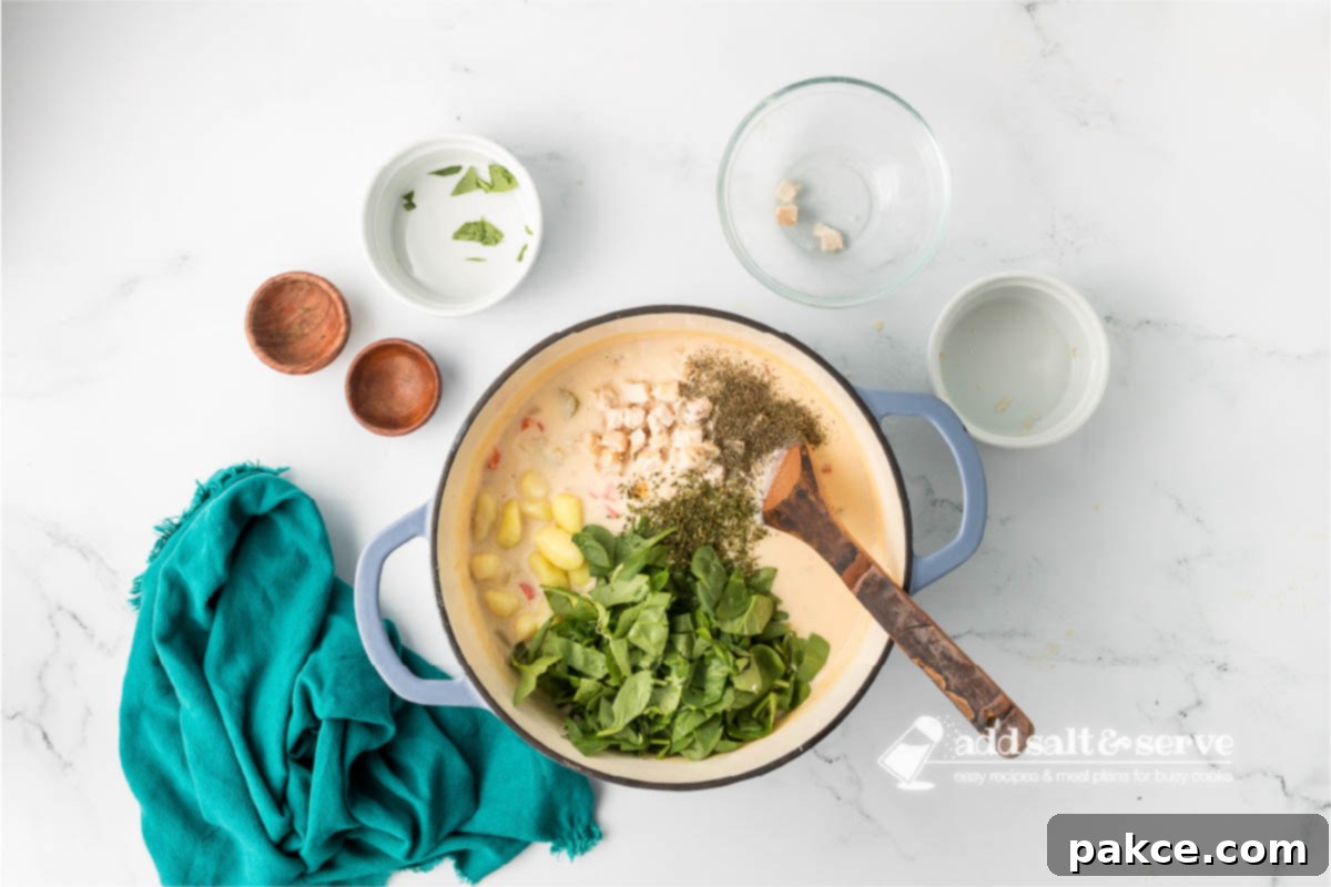 Recreate Olive Garden's Chicken Gnocchi Soup at Home 7 Enamel Dutch oven with Olive Garden Copycat Chicken Gnocchi Soup base with gnocchi, cooked chicken, chopped spinach, and herbs added.
