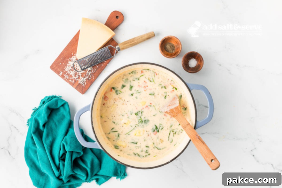 Recreate Olive Garden's Chicken Gnocchi Soup at Home 8 Copycat Olive Garden Chicken Gnocchi Soup in an enamel dutch oven with a wooden spoon in it and a wedge of Parmesan cheese, salt, and pepper beside the bowl.