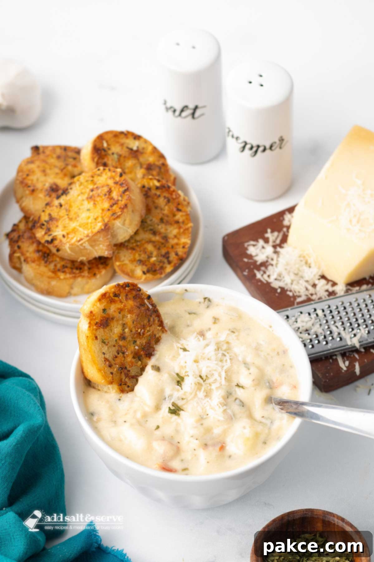 Recreate Olive Garden's Chicken Gnocchi Soup at Home 9 A bowl of Copycat Olive Garden Chicken Gnocchi Soup served with a piece of toasted garlic bread and a wedge of Parmesan cheese with a grater to the side, ready to be enjoyed.