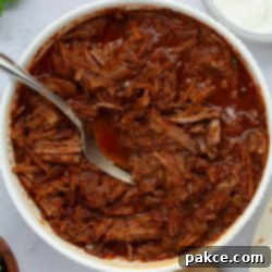 Slow Cooker Shredded Beef Burritos 8 Bowl full of seasoned beef burrito filling with a fork.