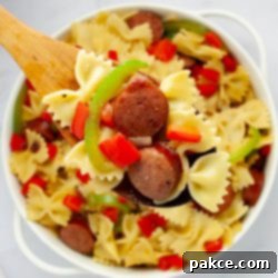 Hearty 20 Minute Kielbasa Pepper Pasta 8 A wooden spoonful of bowtie pasta with red and green bell peppers, red onion, and sliced kielbasa held above a service dish of the same.