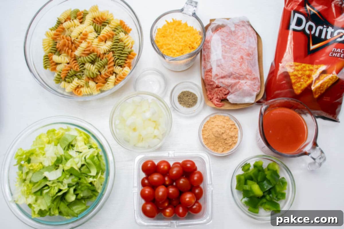 Southwestern Macaroni Toss 3 Overhead shot of ingredients cooked spiral pasta, lettuce, chopped onion, cherry tomatoes, chopped green bell pepper, taco seasoning mix, salt, pepper, shredded cheddar cheese, ground beef, French dressing, and nacho cheese Doritos.