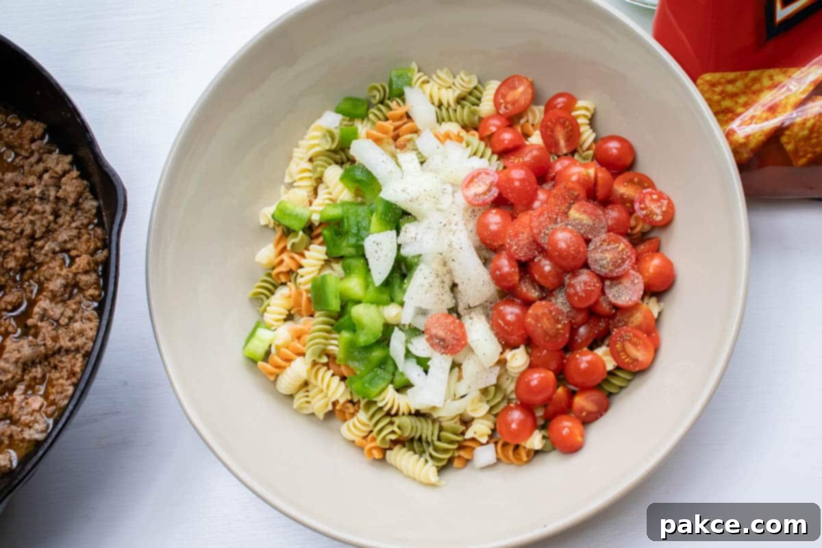 Taco Mac Salad Overhead shot of cooked spiral pasta, chopped green bell pepper, chopped onion, and halved grape tomatoes.