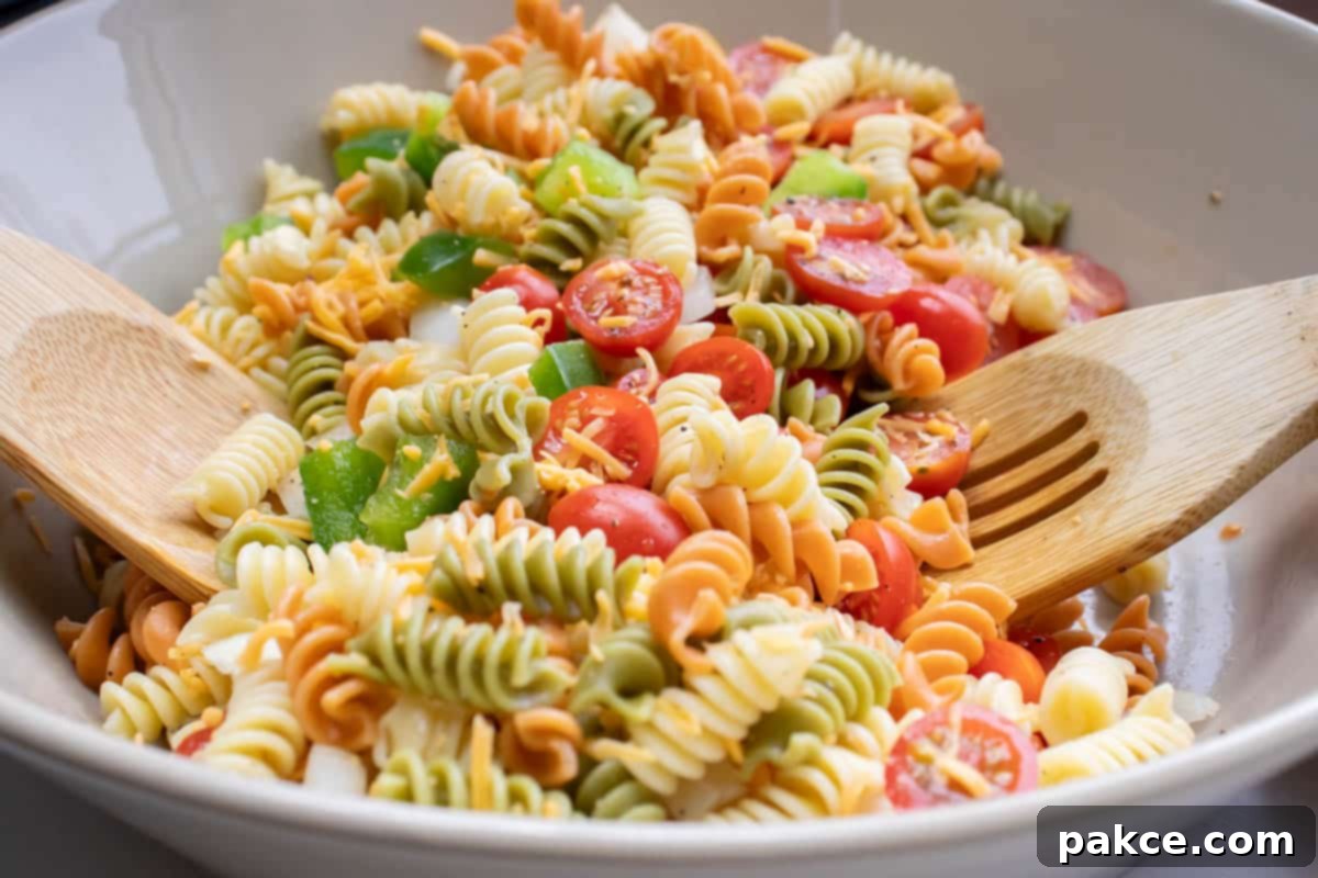 Taco Mac Salad Multi-colored rotini noodles in a bowl with chopped tomatoes and bell peppers and wooden salad spoons.