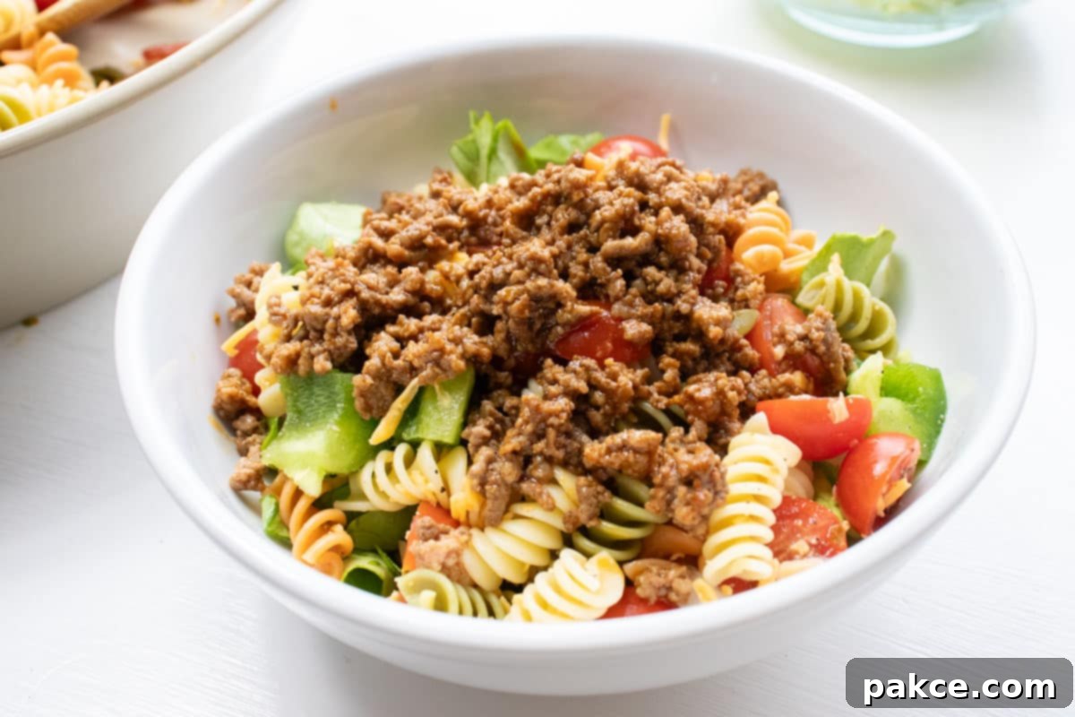 Taco Mac Salad Bowl of seasoned ground beef, spiral pasta, lettuce, and halved tomatoes.