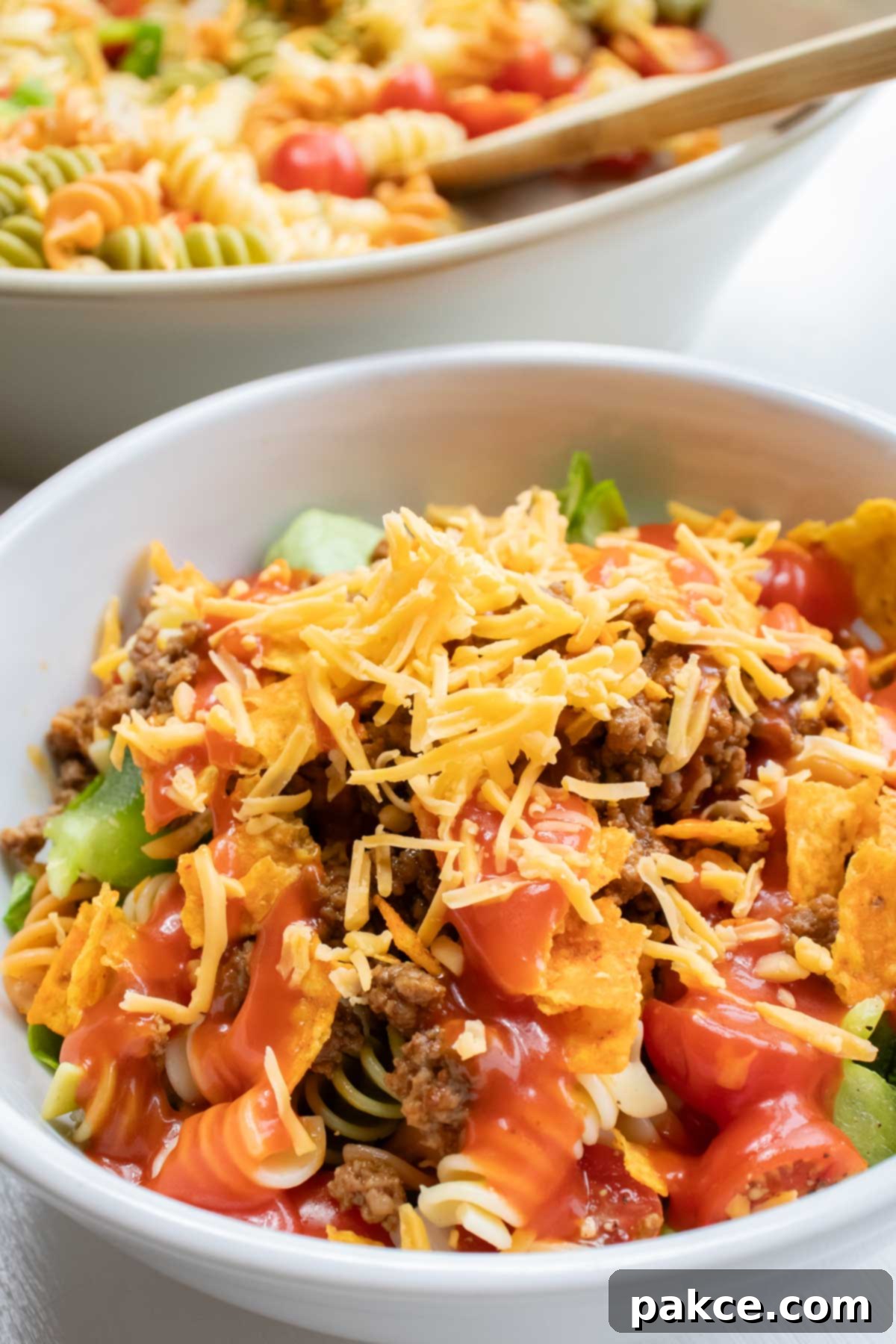 Southwestern Macaroni Toss 4 Bowl of seasoned ground beef, spiral pasta, lettuce, halved tomatoes, nacho cheese Doritos, and French salad dressing with shredded cheddar cheese on top.