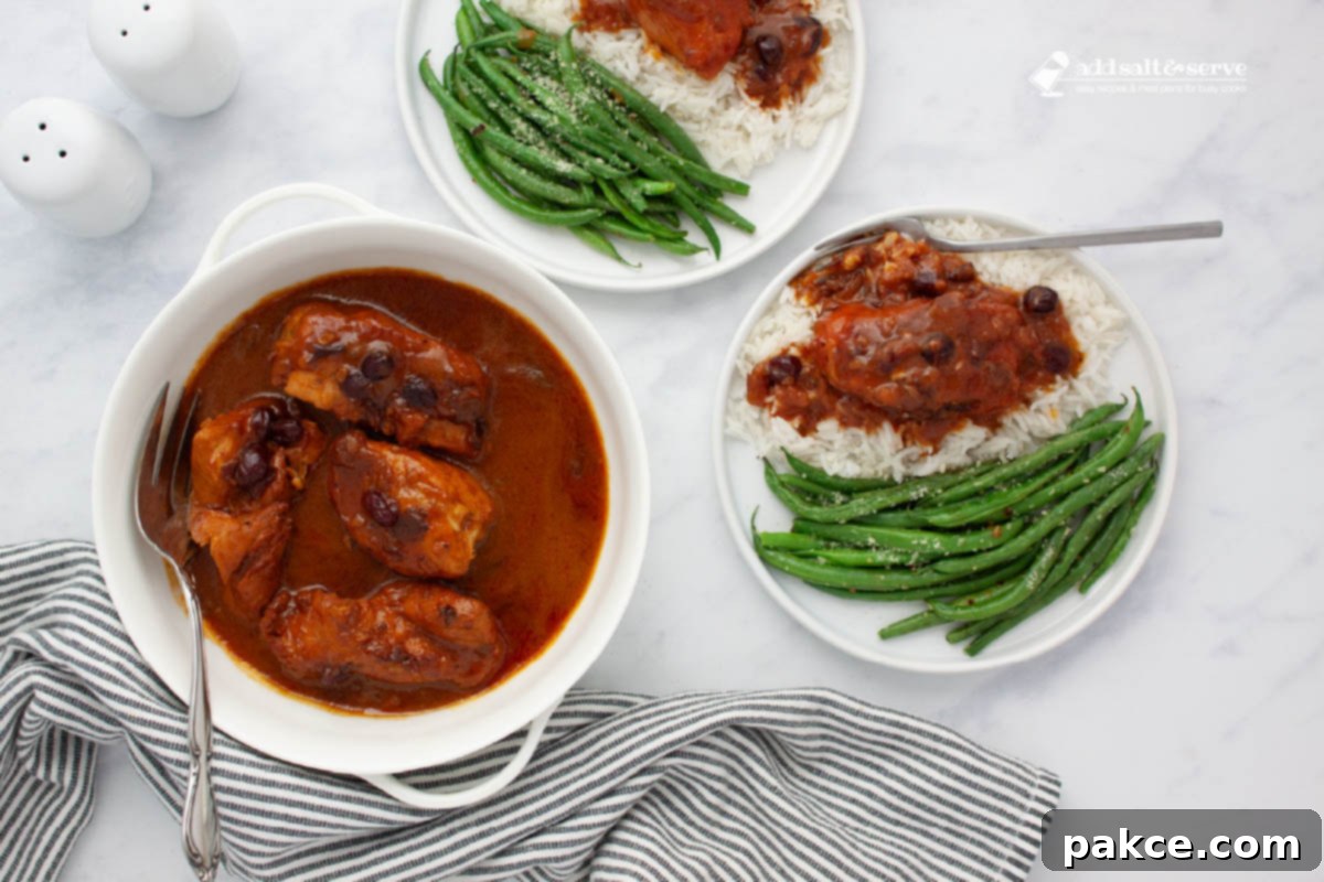 Slow Cooker Zesty Cranberry French Chicken 2 White serving dish with cooked chicken breasts in a sauce made from whole berry cranberry sauce, French dressing, and onion soup mix with a serving fork beside two plates with seasoned green beans and the chicken and sauce over rice on a counter.